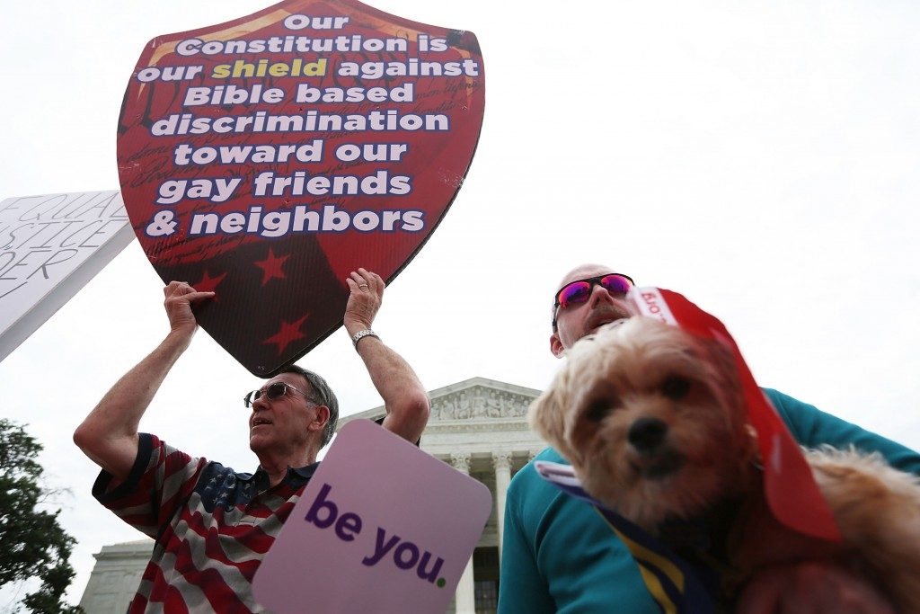 Un hombre sostiene un cartel con la leyenda "Nuestra Constitución es nuestro escudo contra la discriminación basada en la Biblia hacia nuestros amigos gay" en las afueras de la Corte Suprema. 